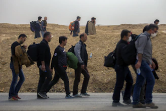 A group of displaced people walking through a rugged landscape carrying their belongings.