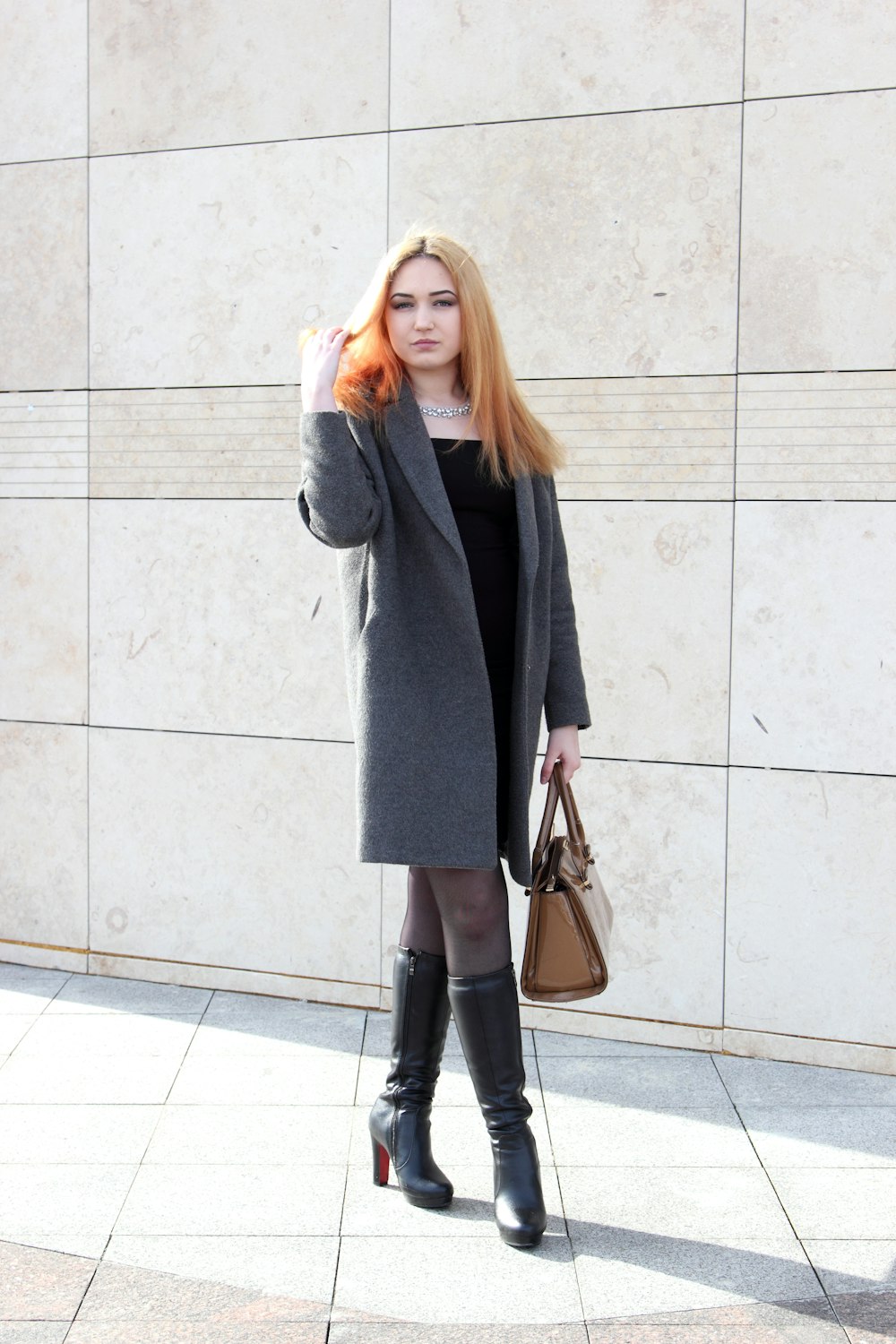 woman standing beside wall while holding her hair during daytime