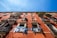 A multi-story building with a terracotta facade, featuring windows and balconies with potted plants. Laundry hangs on a line stretching across the front of the building, under a bright blue sky.