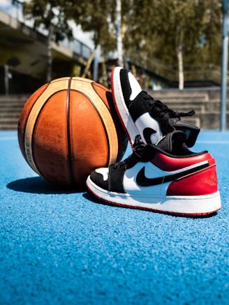Basketball sneakers on a court with a ball nearby.