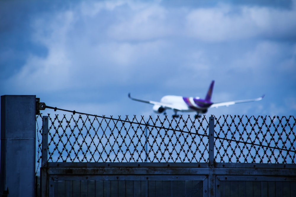 a large jetliner flying over a metal fence
