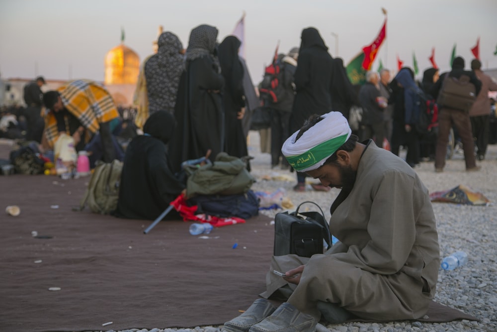 man sitting on ground wearing gray thobe dress