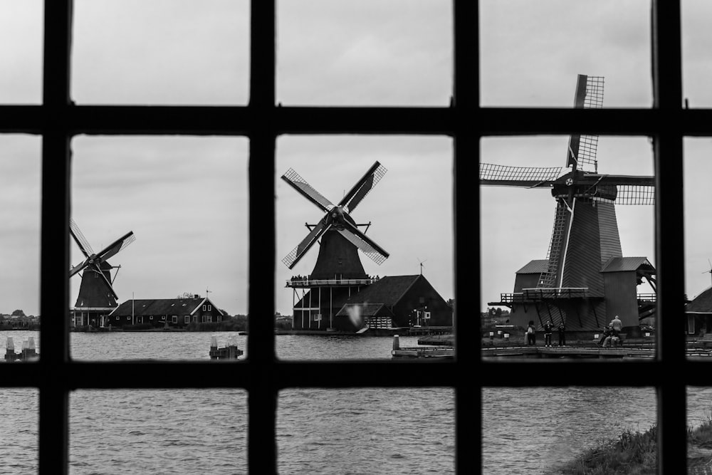 grayscale photo of windmill near body of water