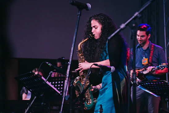 Saxophonist passionately playing under warm stage lights with a lively crowd in the background.