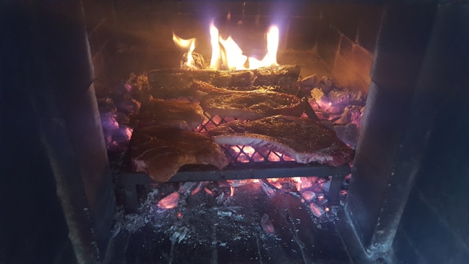 Cozy rustic dining area with glowing embers and sizzling grilled meats on the barbecue.