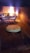 A wood-fired oven interior with a pizza being baked on the brick floor. The flames and embers provide an authentic, rustic cooking environment. The pizza appears to be a simple cheese variety, partially melted and starting to bubble.
