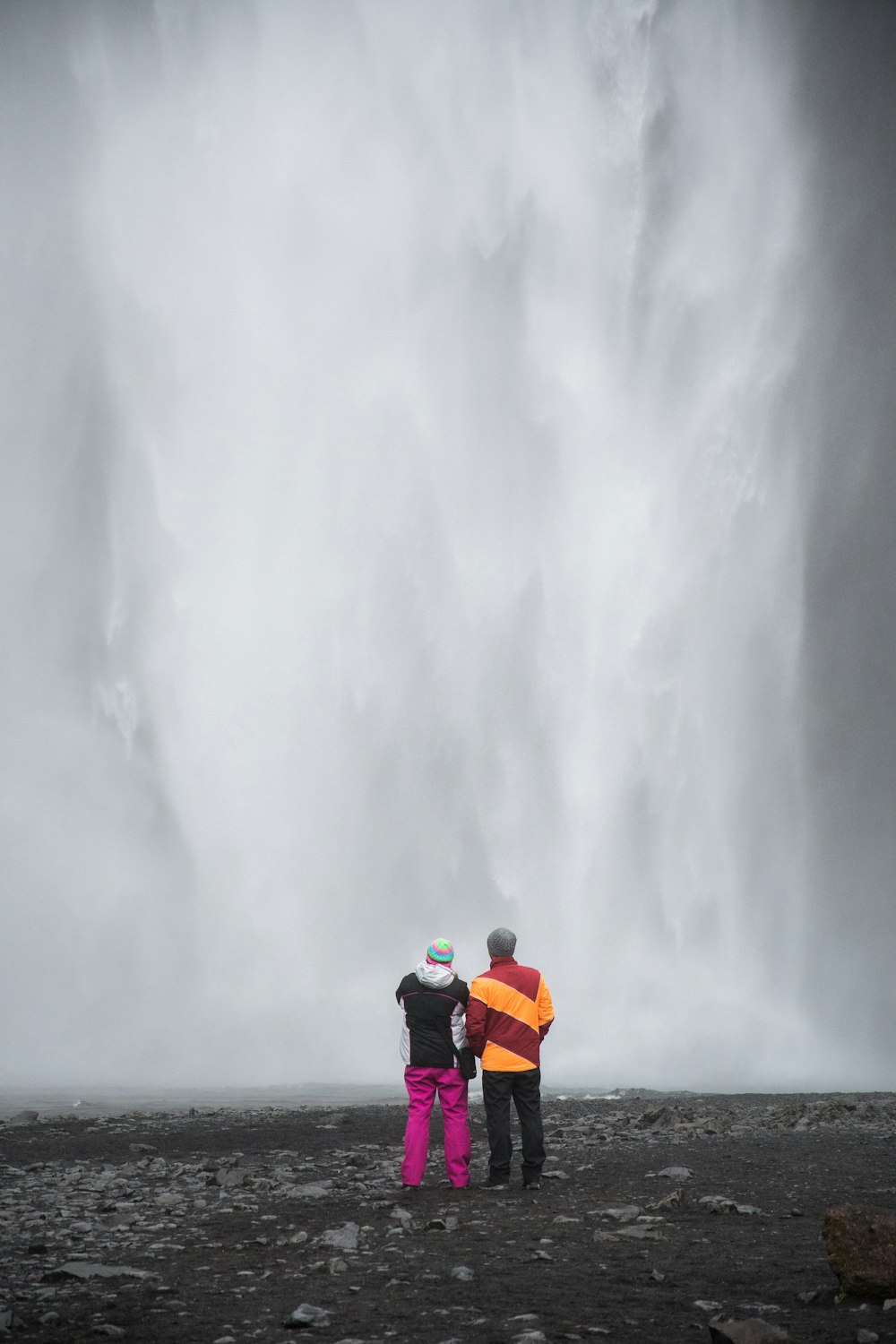 two person standing front of waterfalls