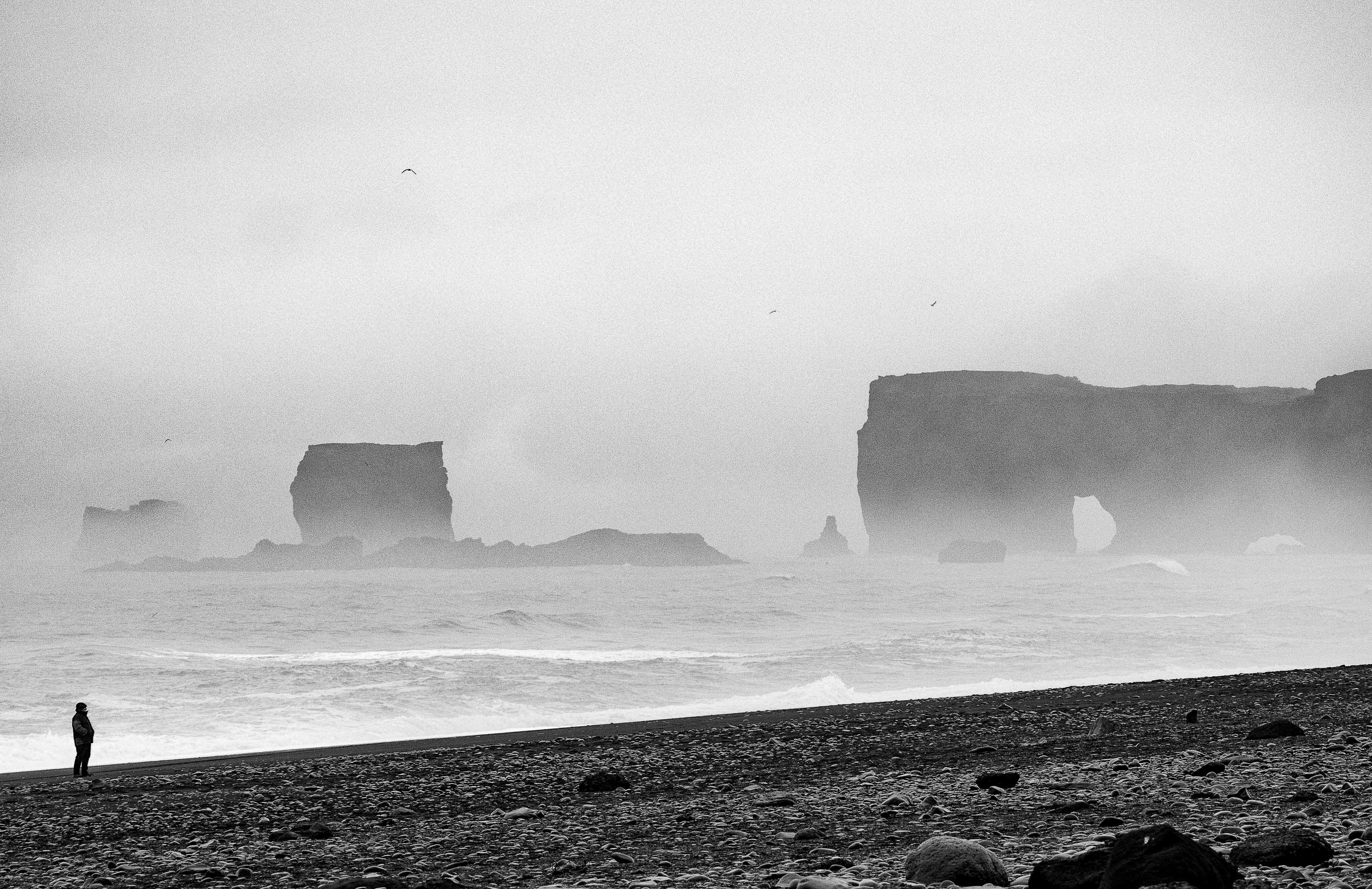 grayscale photography of person standing by the seashore during daytime