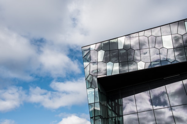 A modern building with a unique glass facade featuring hexagonal patterns that reflect the cloudy sky. The architecture gives a sense of innovation and artistic design.
