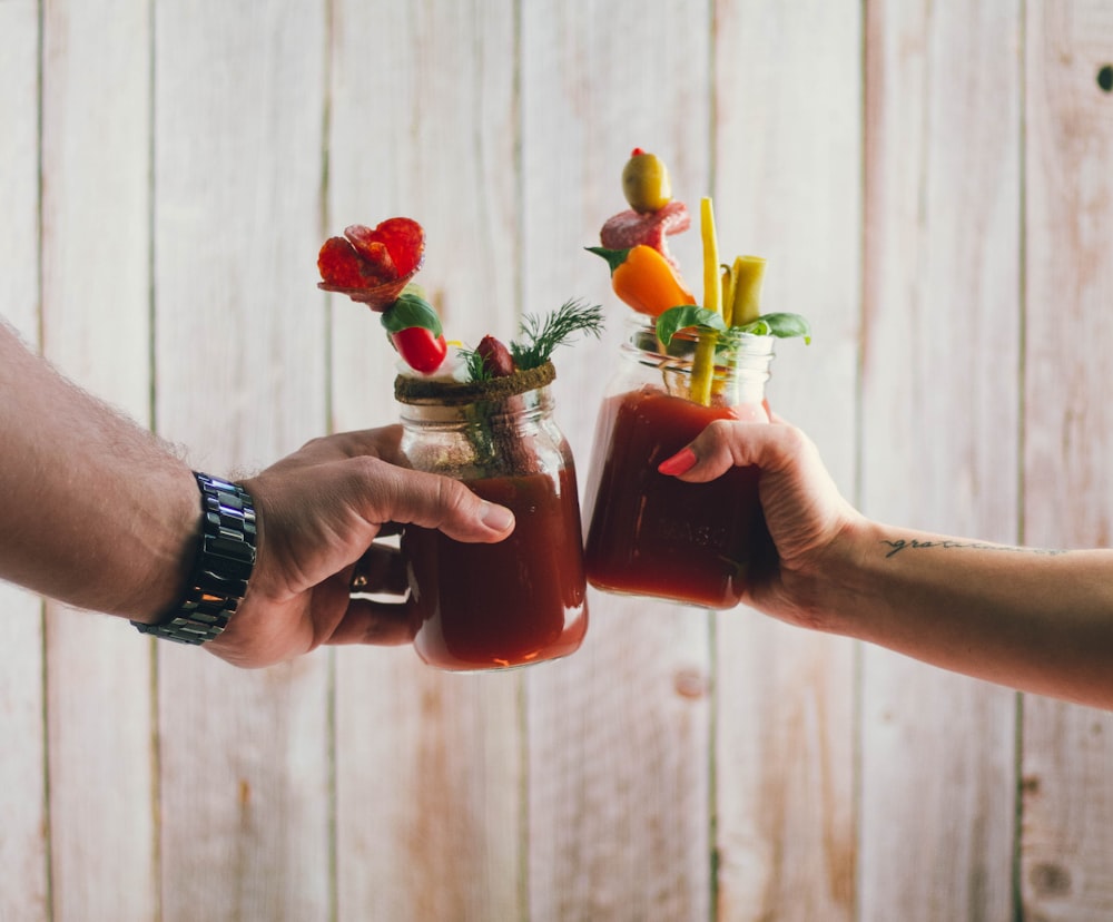 two person holding filled clear glass jars