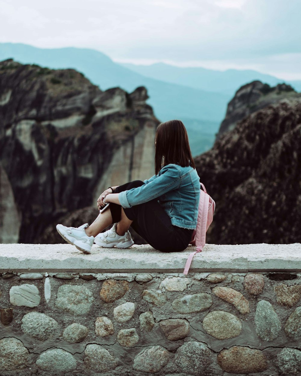 woman sitting on top of brick wall facing the mountains