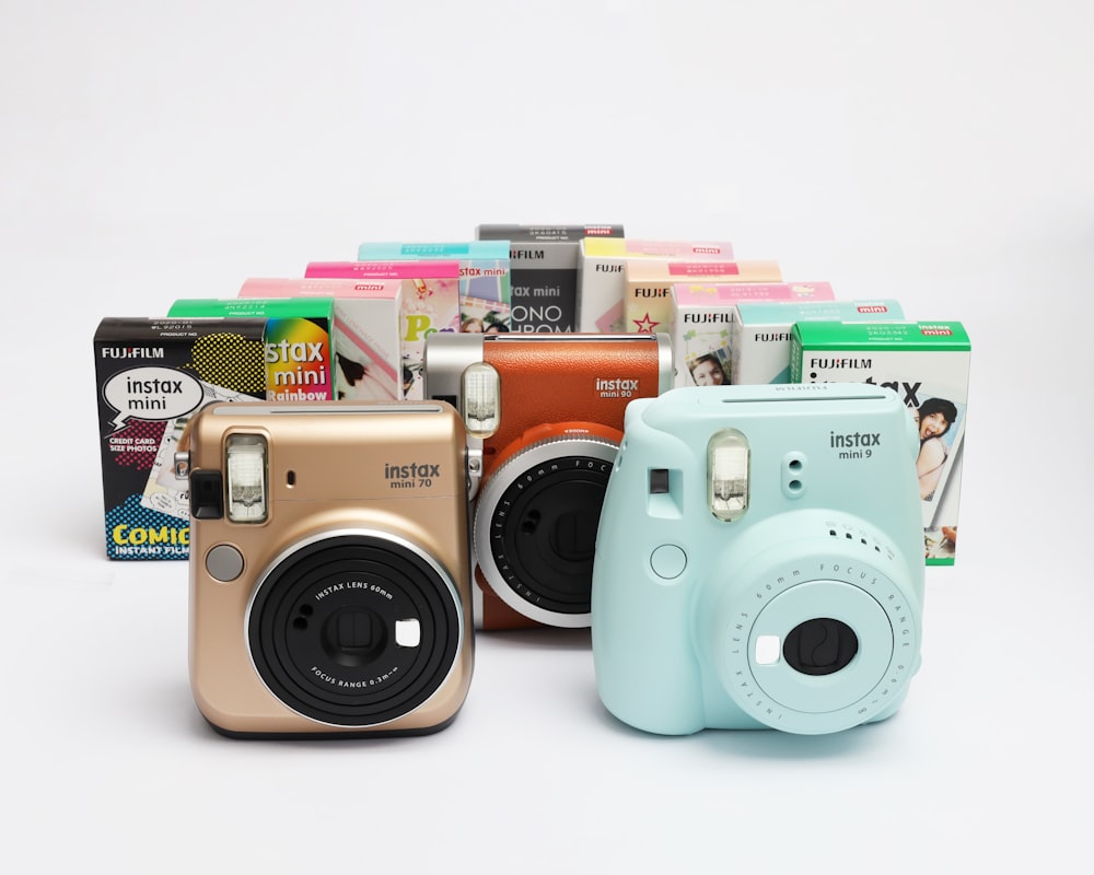 three Fujifilm Instax instant cameras with film paper boxes