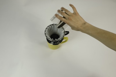 A beige ceramic pour-over dripper with fresh coffee dripping into a brown mug.