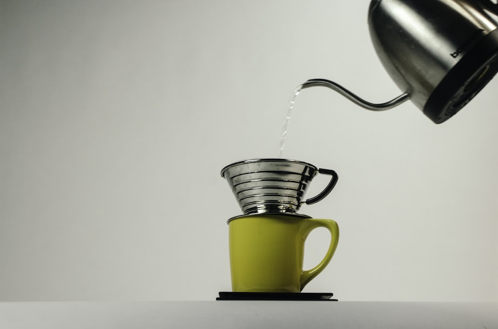 kettle pouring water on gray stainless steel cup on top on yellow ceramic mug