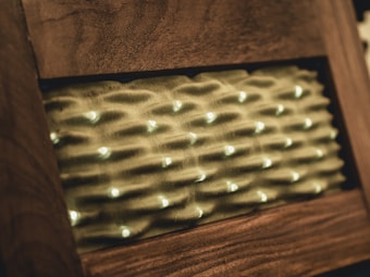 A rectangular wooden frame with a textured surface inside, featuring a pattern of wavy ridges and scattered light spots that appear to be some form of lighting.
