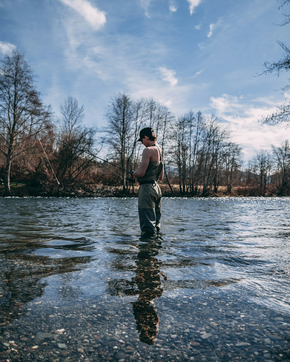 person standing on body of water while holding fishing rod during daytime