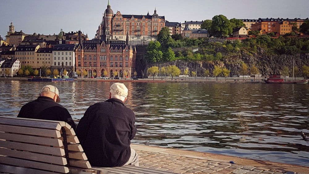 two man sitting on bench facing on body of water during daytime