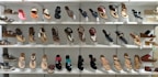 A display of various women's sandals arranged neatly on white shelves. The sandals are diverse in style, including flip-flops, strappy sandals, and wedges, showcasing a range of designs from casual to more decorative options.