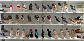 A display of various women's sandals arranged neatly on white shelves. The sandals are diverse in style, including flip-flops, strappy sandals, and wedges, showcasing a range of designs from casual to more decorative options.