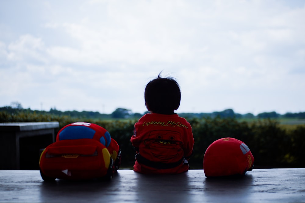 toddler sitting beside red car plush toy outdoors