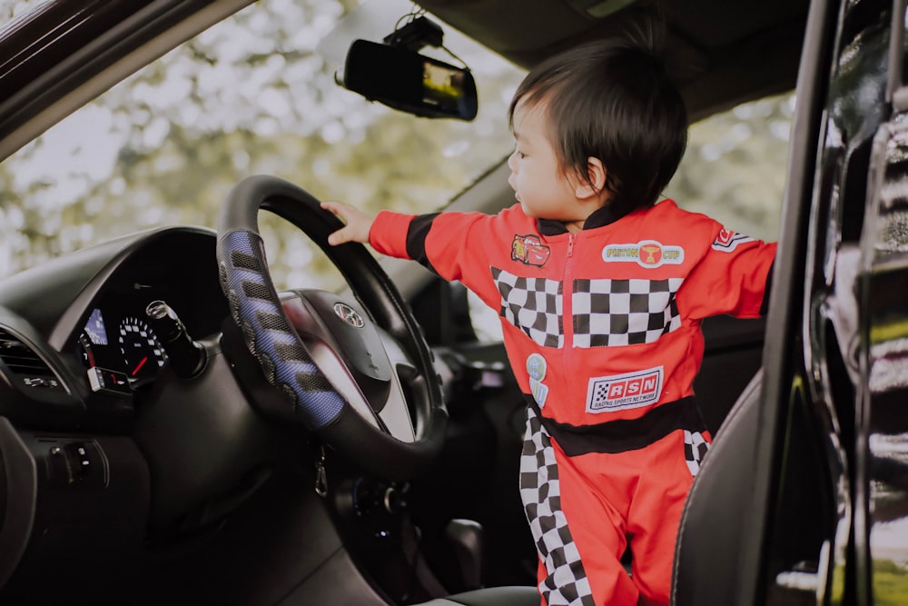 male toddler standing on driver's seat of a car