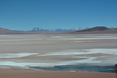 A panoramic view of the vast Atacama Desert under a clear blue sky, with rugged salt flats and distant volcanoes.