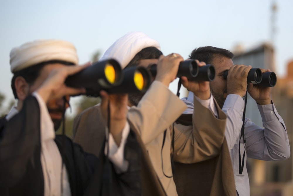 three men using binoculars