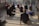 Several people are positioned on a reflective floor in a well-lit room, performing a yoga pose. They are arranged in a spread-out formation, each with a focused and serene expression, looking upward as they stretch their bodies.
