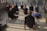 Several people are positioned on a reflective floor in a well-lit room, performing a yoga pose. They are arranged in a spread-out formation, each with a focused and serene expression, looking upward as they stretch their bodies.