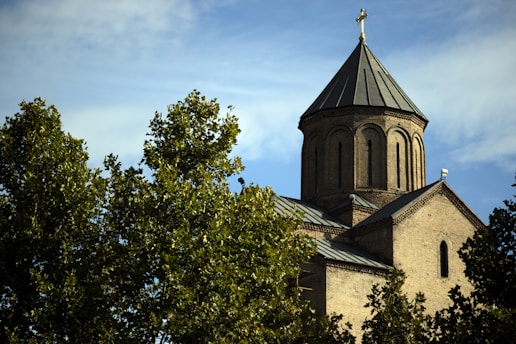 A serene church building surrounded by lush greenery under a clear blue sky.