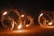 Performers engage in a fire dance, skillfully twirling large fiery torches in circular motions, creating captivating patterns of light against a dark backdrop. The bright flames and flying sparks illuminate their movements as an audience watches the mesmerizing display.