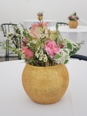 An aluminium vase in a gold finish, holding fresh flowers on a wooden table.