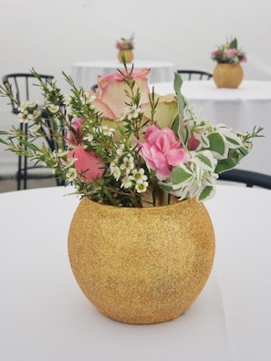 An aluminium vase in a gold finish, holding fresh flowers on a wooden table.