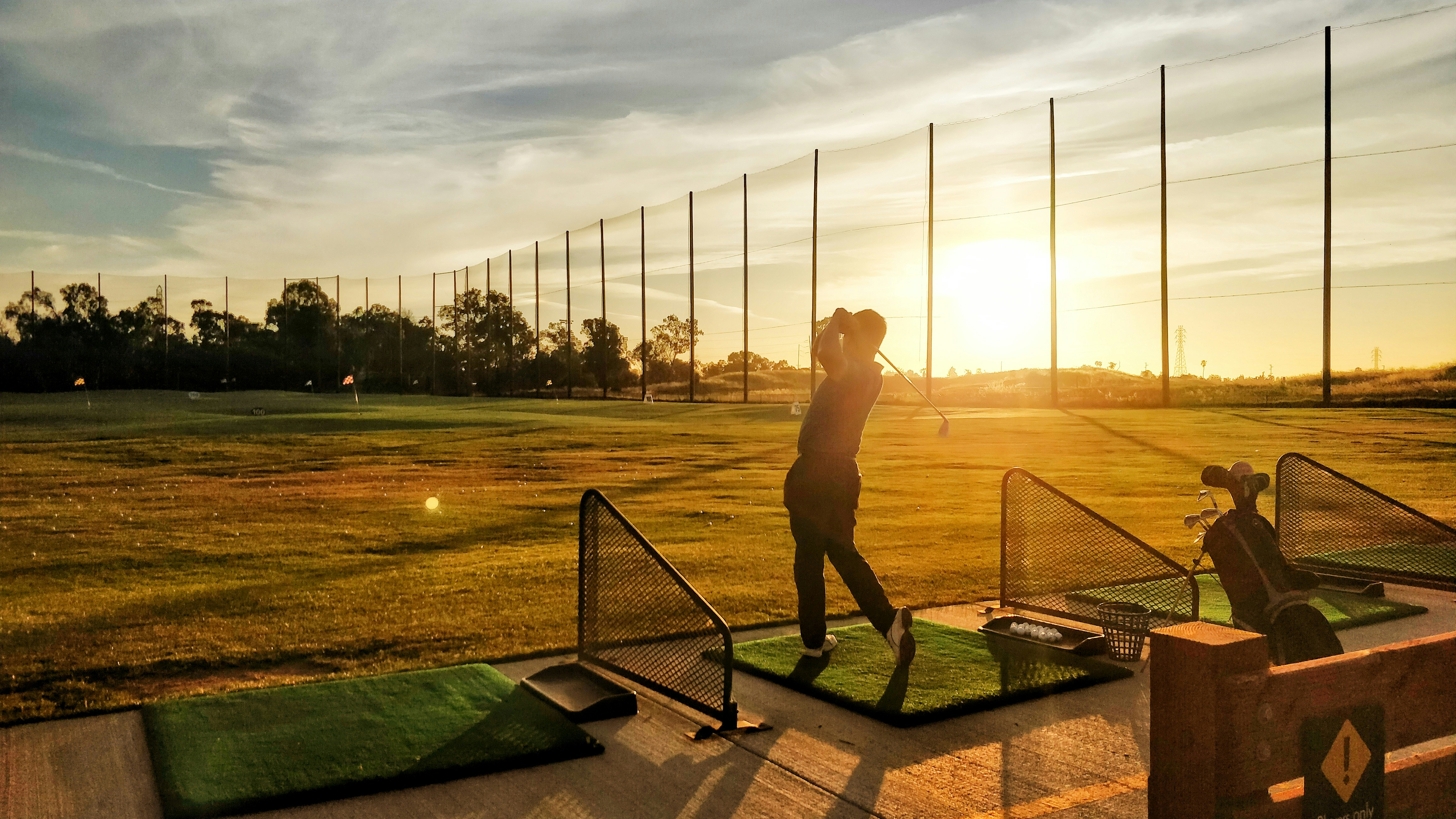 Golfer at a driving range hitting a ball with perfect form, warm evening light