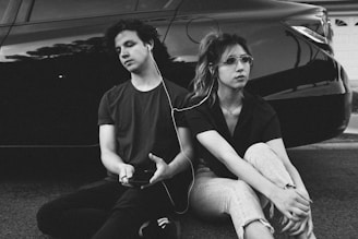 grayscale photo of man and woman leaning on vehicle