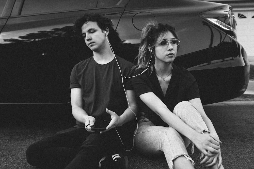 grayscale photo of man and woman leaning on vehicle