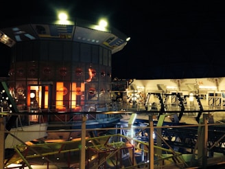 A futuristic, sci-fi interior setting with a distinctive circular structure featuring illuminated panels and a grid of circular designs. The scene includes metallic railings and complex machinery, suggesting a high-tech environment. The lighting is predominantly dim with several warm, glowing lights adding to the ambiance.