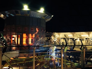 Estrutura industrial iluminada à noite com luzes alaranjadas e amarelas em ambiente futurista.