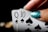 A close-up of two playing cards showing the Queen and 10 of spades held by a hand with glittery teal nail polish.