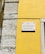 A street sign is mounted on a vibrant yellow wall next to a section of exposed stonework on a building. The sign reads 'Rua da Conceição da Glória' and is attached to the wall with visible screws.