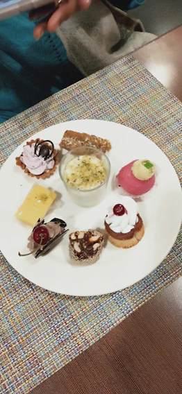 Close-up of an elegant petit four assortment with delicate gold accents on a cream-colored plate.