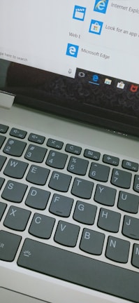 A close-up view of a laptop keyboard and a computer screen displaying the start menu with icons for Internet Explorer and Microsoft Edge, along with a search bar entry point.