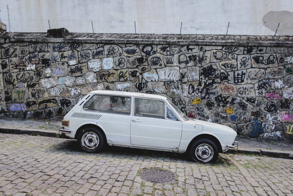 Coche blanco aparcado al lado de la carretera cerca de la pared con mural