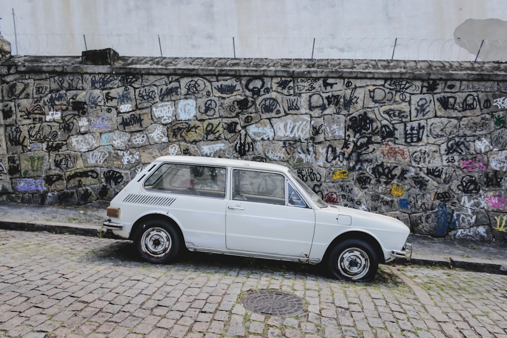 壁画のある壁の近くの道路脇に停車している白い車