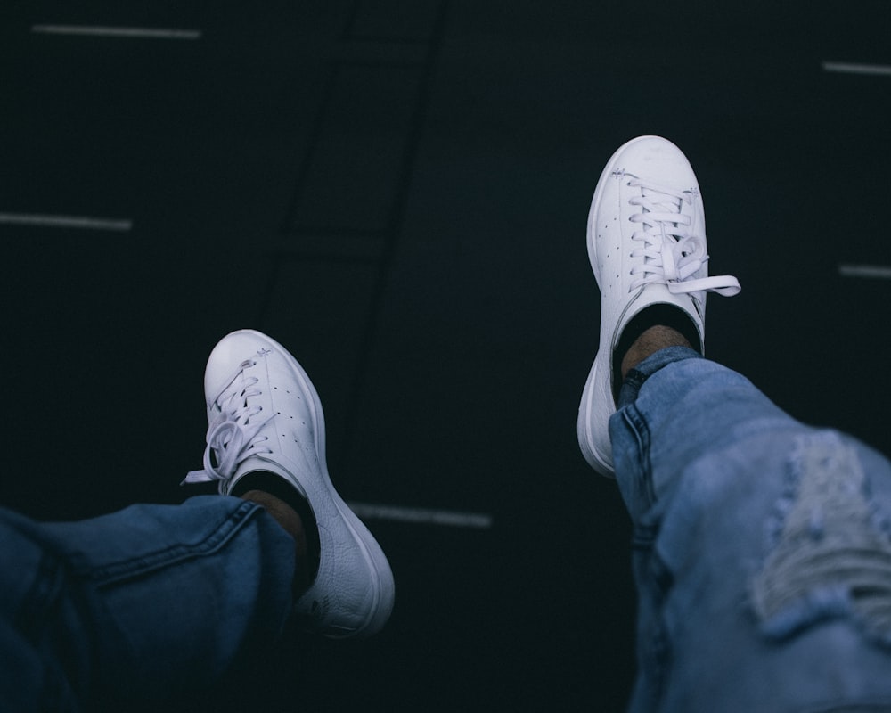 person wearing distressed blue denim jeans and white low-top sneakers