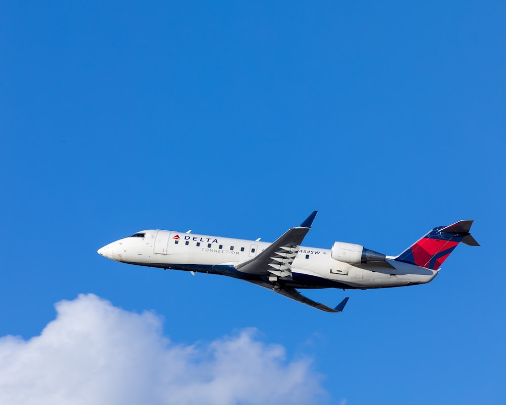 白と青の曇り空の下を飛行する白、青、赤のデルタ航空旅客機