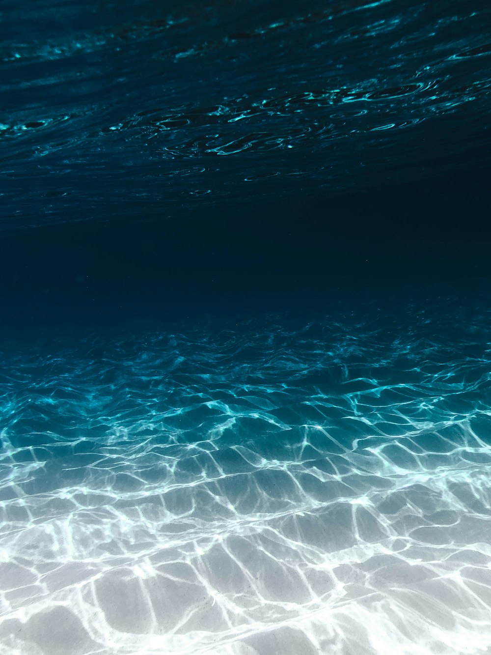 grauer Sand unter blauem, klarem Wasser