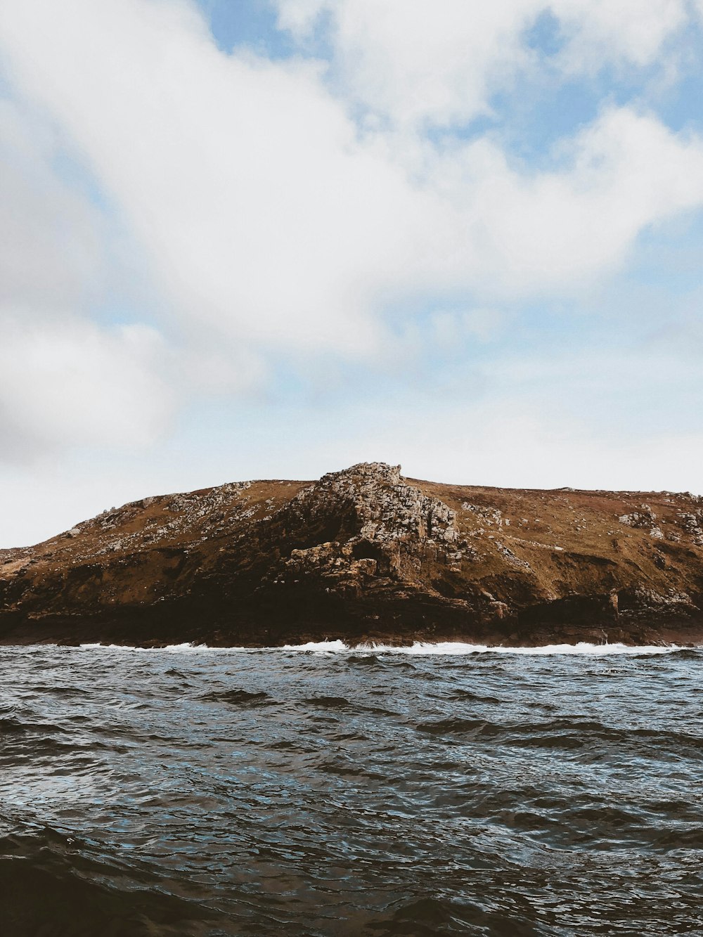 green hill covered with boulders near sea water during cloudy day