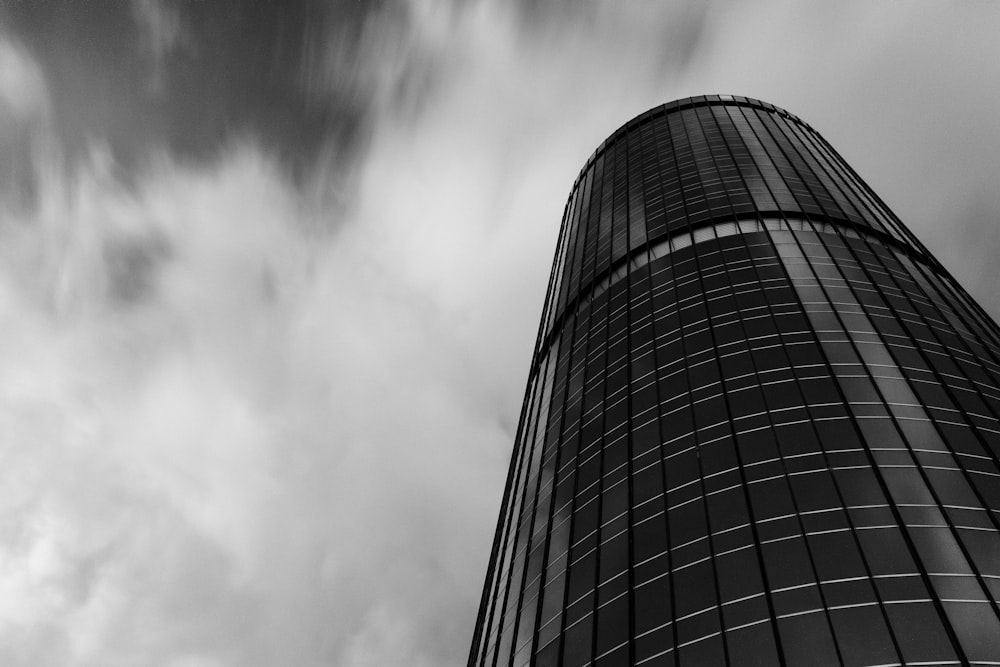 grayscale low angle photography of tubular building under cloudy sky