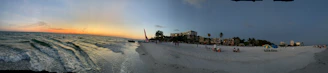A panoramic shot of a sunset over a tranquil beach, with tourists relaxing and enjoying the view.